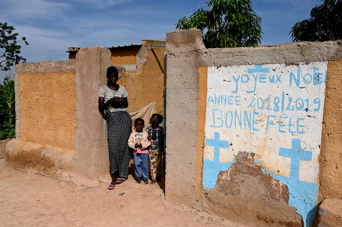 A woman and children stand at a fence next to a mural ' in the village of Yagma, north of Ouagadougou, the capital of Burkina Faso, on Sept. 17, 2019.