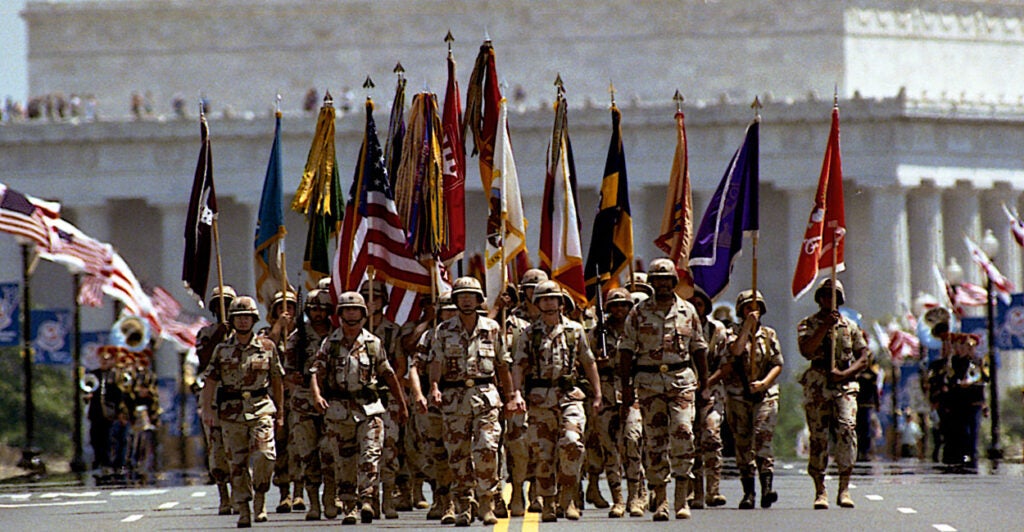 A unit of soldiers march toward camera in front of Lincoln Memorial during the Desert Storm Victory Parade in 1991. In the background, a military band.
