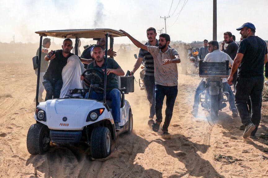TOPSHOT - Palestinians transport a reportedly captured Israeli person, in Khan Yunis in the southern Gaza Strip, on October 7, 2023. One month after Israel was wracked by Hamas attacks, life has been upended for both the Palestinians and Israel after it launched a war of reprisal in the Gaza Strip. The October 7 attacks by Hamas militants who stormed across from Gaza and struck kibbutzim and southern Israeli areas killed 1,400 people, mostly civilians, and deeply scarred the nation. The health ministry in Hamas-run Gaza says nearly 9,500 have been killed, two-thirds of them women and children, and mostly civilians. (Photo by AFP) (Photo by -/AFP via Getty Images)