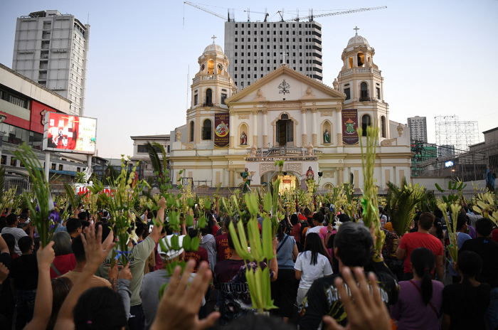 Catholic faithful raise their palm fronds during the blessing in front of a church as part of the traditional lenten devotion on Palm Sunday in Manila on March 24, 2024.