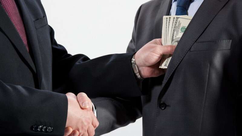 Two men in business suits shake hands, while one places cash in the other's jacket pocket. | Zestmarina | Dreamstime.com