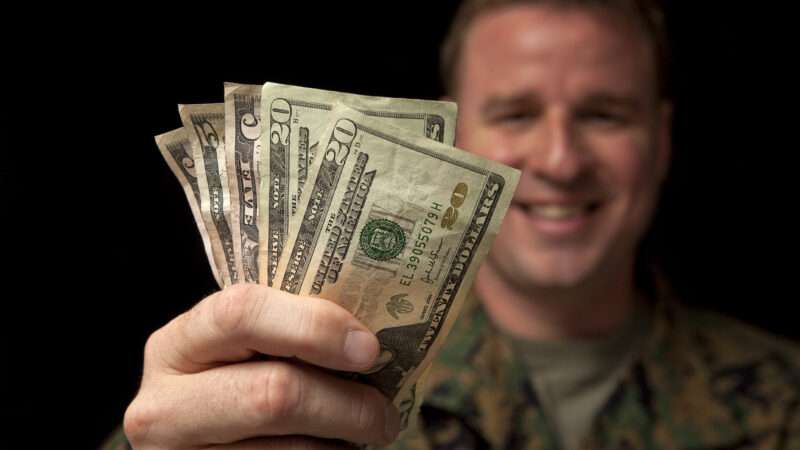 A man in U.S. Army fatigues happily holds up a handful of American money. | Elswarro | Dreamstime.com