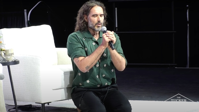 A barefoot Russell Brand kneels in prayers at the conclusion of an event with Tucker Carlson in Phoenix, Arizona, on Sept. 4, 2024.