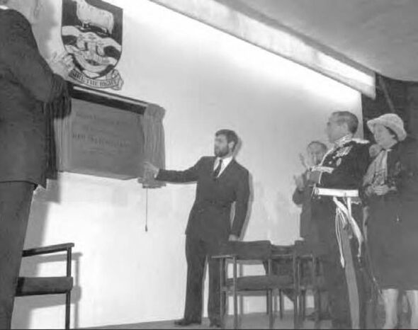 Man unveils wall plaque with other watching on Man unveils wall plaque with other watching on