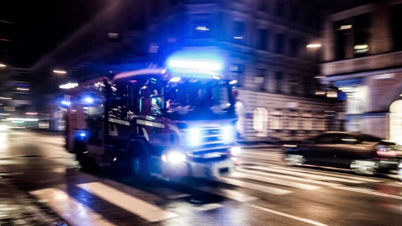 A fire truck driving fast through a city at night with its lights on. | Mino Surkala | Dreamstime.com
