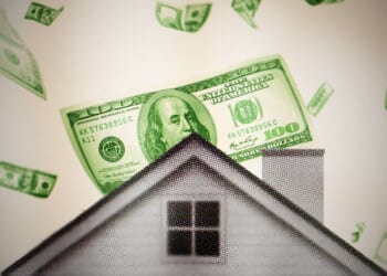 A house is seen with $100 bills falling behind it