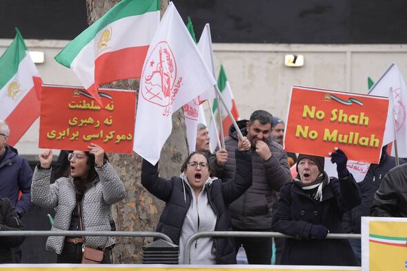 A group of people, some of whom are holding placards and flags, are gathered in an outdoor setting. They appear to be participat