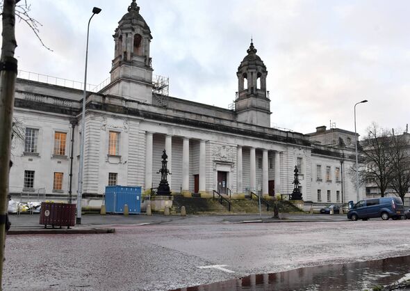 An imposing classical-style building with two prominent towers and a series of columns, situated in an urban setting with a pave