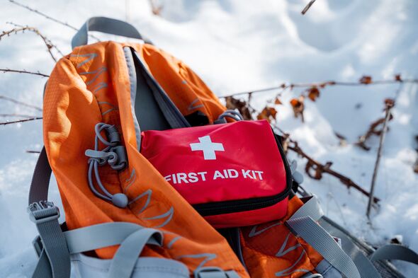An orange backpack accompanied by a first aid kit is resting on a blanket of snow, highlighting the importance of being thoroughly prepared for winter