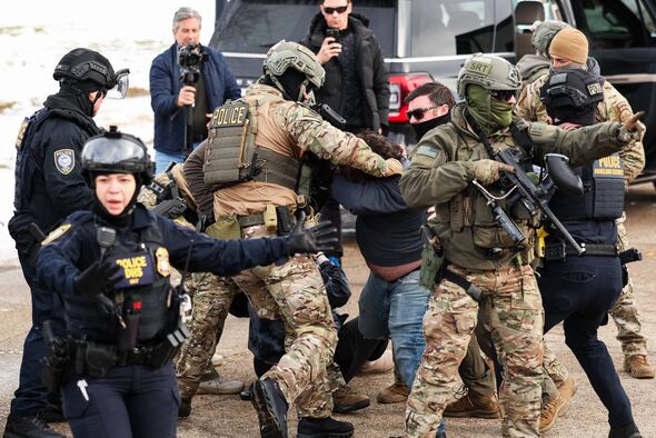 A group of individuals dressed in tactical gear, including helmets and firearms, appears to be engaged in a physical altercation