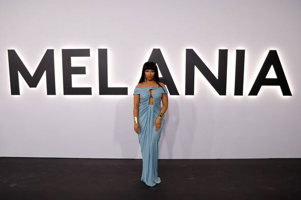 An individual dressed in a blue gown is standing before a large backdrop featuring the word 
