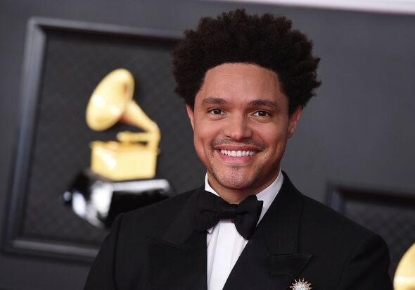 An individual dressed in formal attire, including a tuxedo and bow tie, stands against a backdrop featuring a Grammy Awards embl