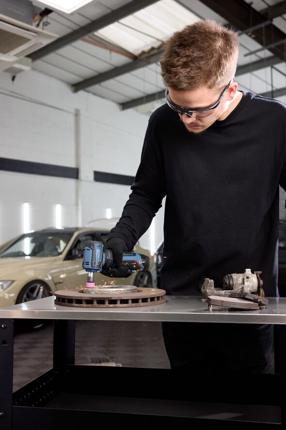 Man wearing safety goggles uses a tool in a garage