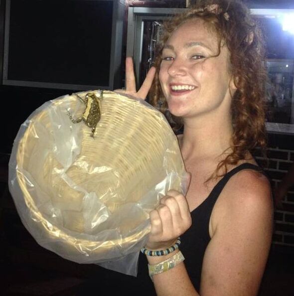 An individual with curly hair is holding up a circular object containing a small insect, smiling brightly.