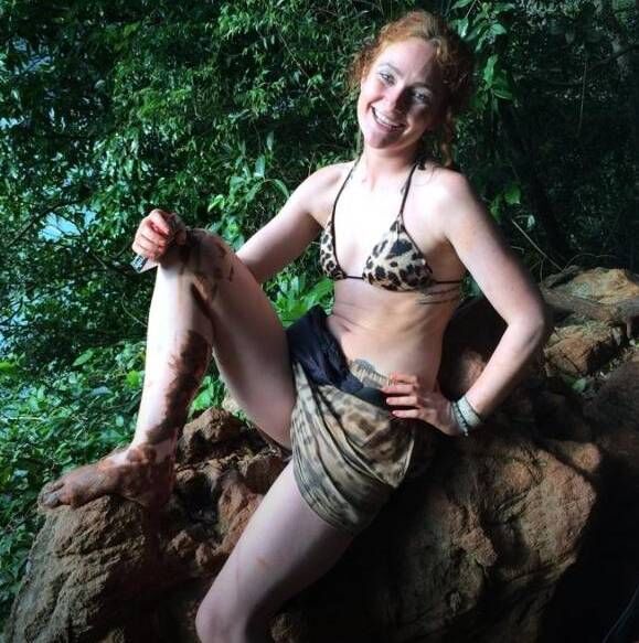 An individual is seated on a natural rock formation, situated in a verdant and lush forested area. The person is dressed in a pa