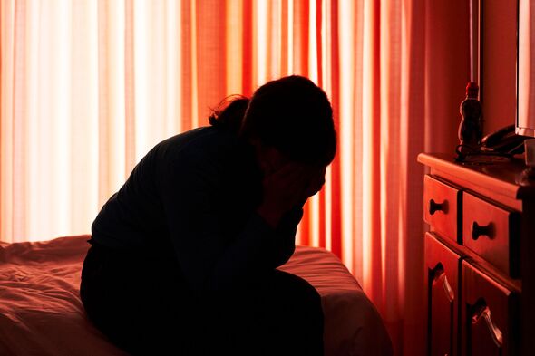 A woman sitting on a bed in a room with her hands on her face, her silhouette is visible because it A woman sitting on a bed in a room with her hands on her face, her silhouette is visible because it
