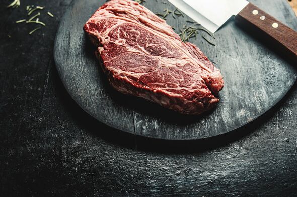 Close up of raw marbled chuck eye beef steak on black cutting board with butcher knife Close up of raw marbled chuck eye beef steak on black cutting board with butcher knife