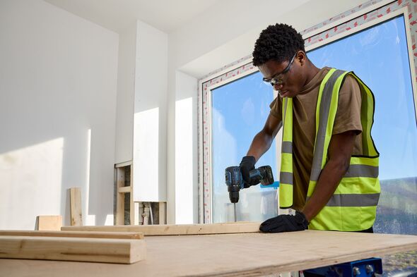 Man in a hi-vis jacket drills into a wooden board