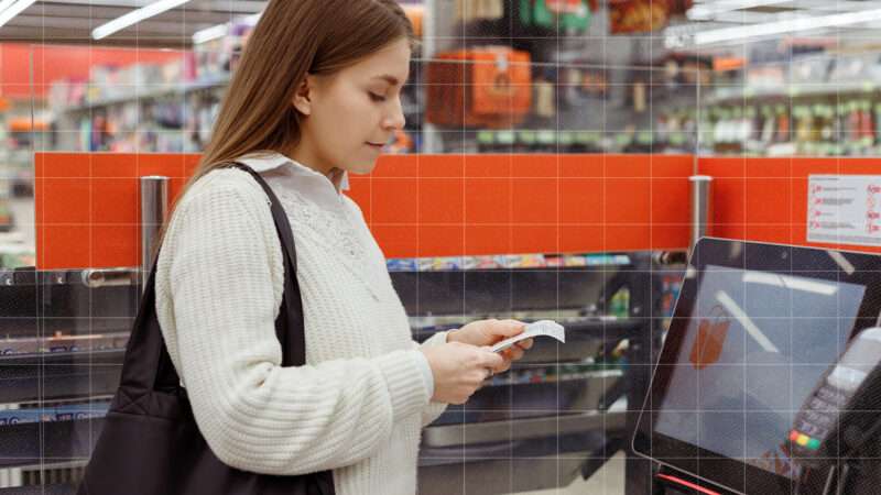 A woman shopping in a grocery store checks her receipt after using a self-checkout. | Envato