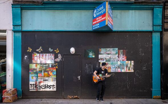 A man plays the guitar near the doorway of a closed and boarded-up shop on March 2, 2026 in Newport, Wales