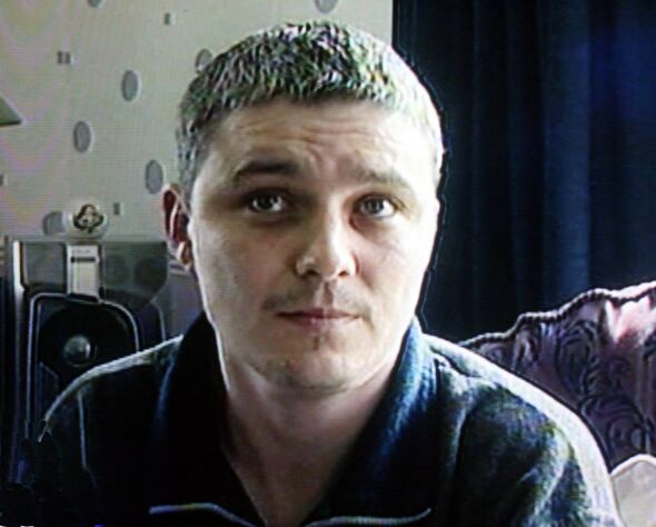 An individual with short hair is sitting in an indoor setting, possibly a living room. The person is wearing a dark-colored shir