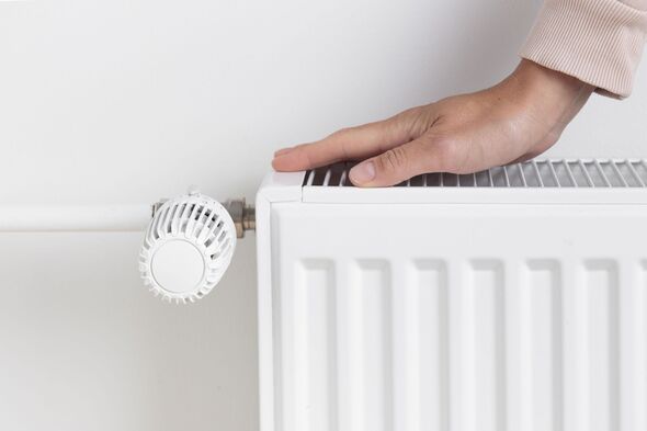 Woman warming hand near heating radiator at home, resource management during colder seasons
