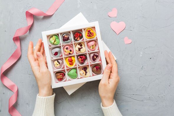 Female hands with delicious candies in box on color background