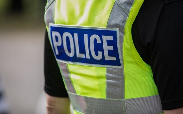 A stock image of a police officer seen from behind wearing a hi-viz vest which says 'police' on the back