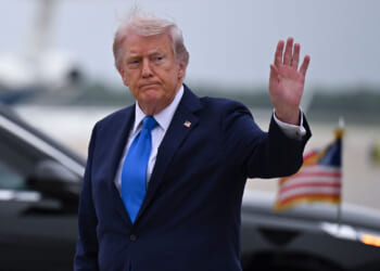 President Donald Trump waves to reporters at an airport.