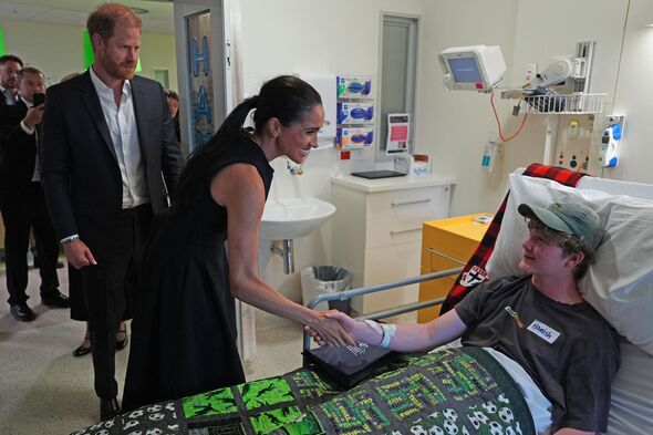 Meghan Markle shakes hands with a patient as Prince Harry looks on during a hospital visit