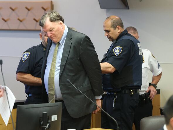 An individual in formal attire, consisting of a suit and tie, is observed standing and appears to be conversing with two law enf