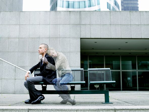 Two individuals are seated on a bench situated on an urban street, engaged in conversation. The bench is positioned on a concret